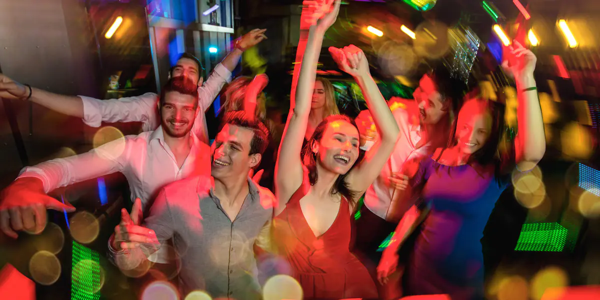 Energetic group dancing at a nightclub with colorful bokeh lights.