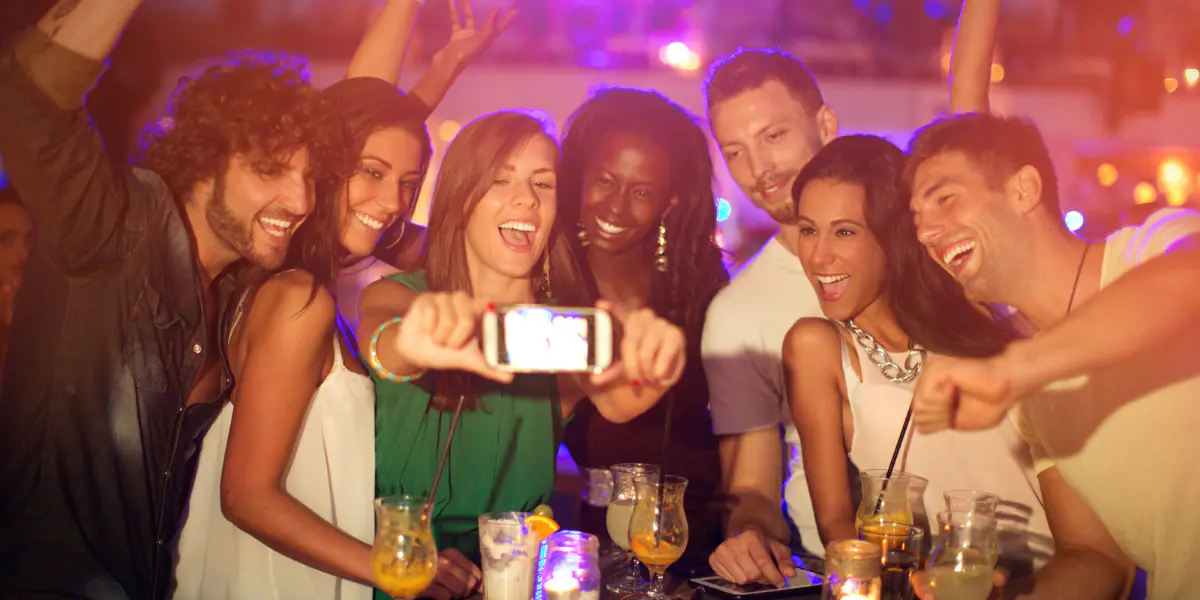 Friends taking a group selfie at a lively bar or party.